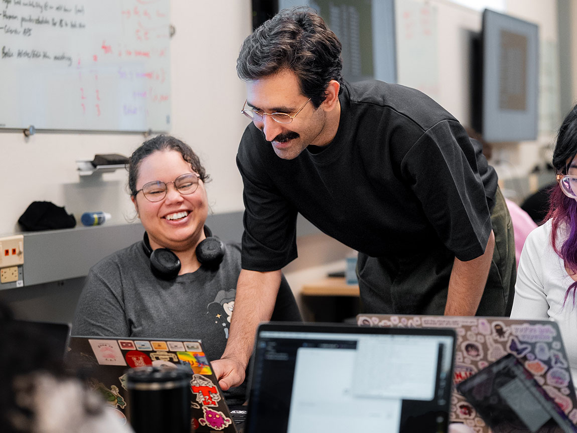 A college professor in a black T-shirt helps a student on the computer